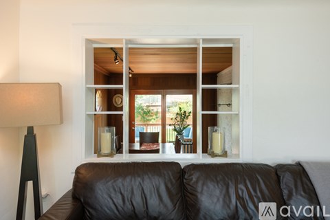 A black couch sits in front of a window with a lamp to the side.