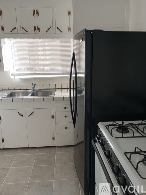 A black refrigerator stands next to a white stove in a kitchen.