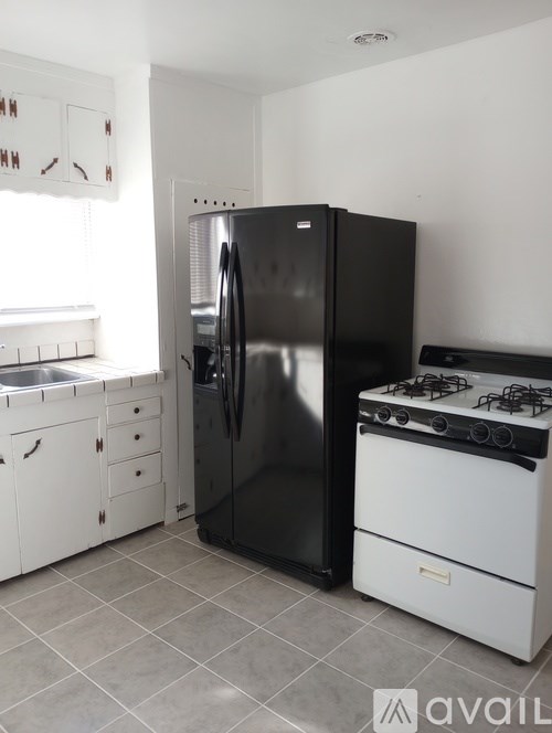 A black refrigerator stands in a kitchen next to a white stove.