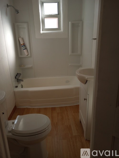 A white toilet sits in a bathroom with a white tub and a window.