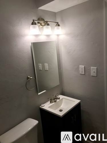 A bathroom with a toilet, sink, mirror, and light fixture.