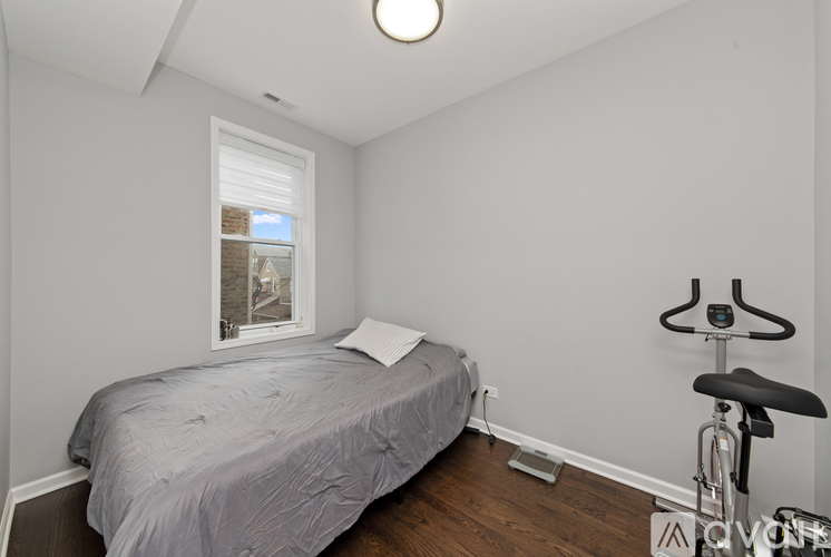 A bedroom with a bed, a window, and a stationary exercise bike.