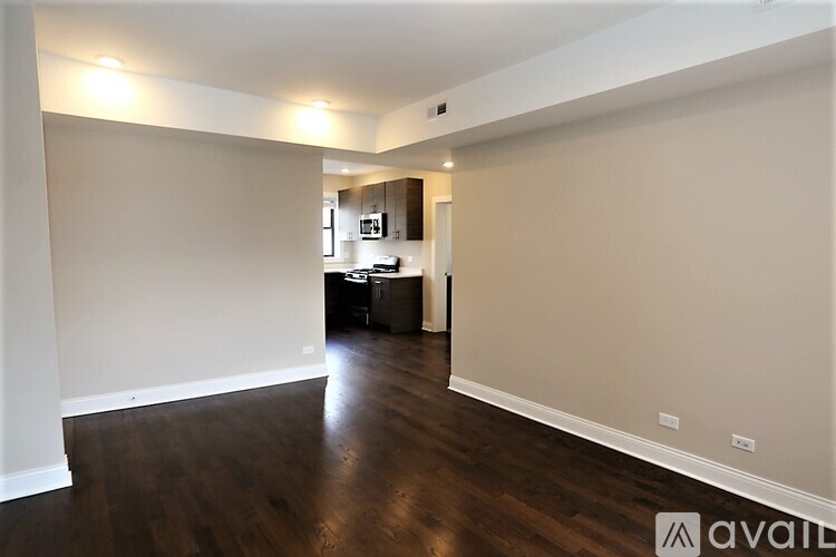 A spacious room with wooden floors and a kitchen area in the background.