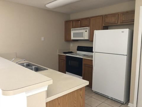 A white refrigerator stands in a kitchen with wooden cabinets and a countertop.