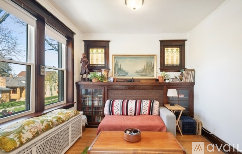 A room with a large window, a sofa, a wooden table, and a painting on the wall.