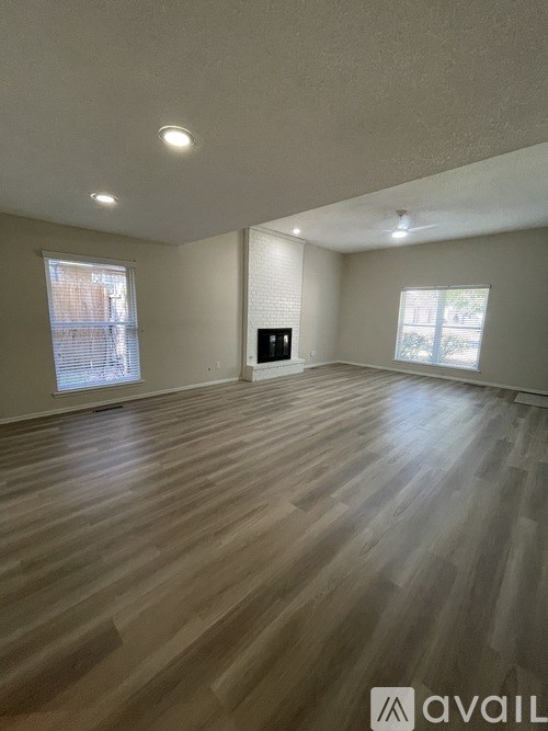 A spacious room with wooden flooring and two windows.