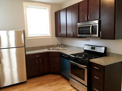 A kitchen with a stainless steel refrigerator, a black stove, and brown cabinets.