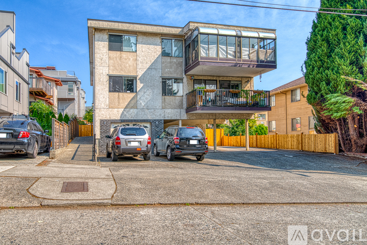 A modern two-story house with a balcony on the upper floor is surrounded by parked cars.