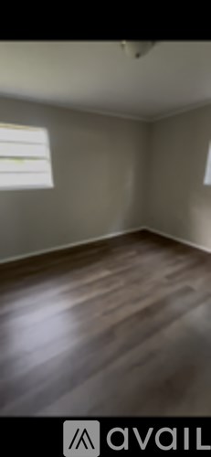 A room with wooden flooring and two windows.