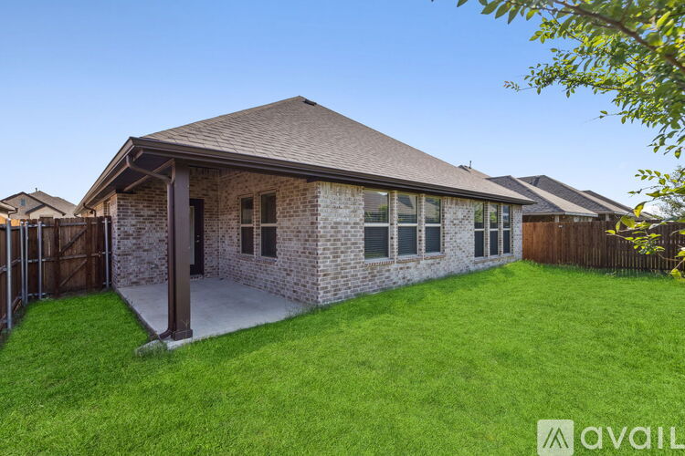 A house with a brown roof and a brick exterior is surrounded by a green lawn.