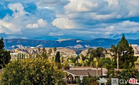 A suburban landscape with houses and trees in the foreground and mountains in the background.