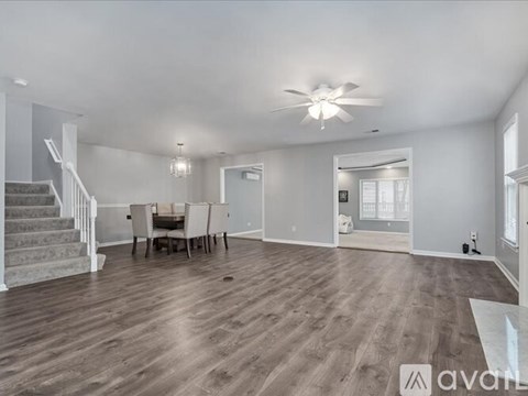 A spacious room with a dining table and chairs, a staircase, and a ceiling fan.