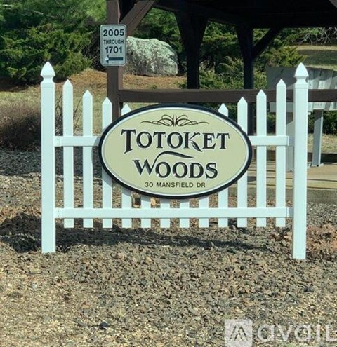 A sign for Totoket Woods is in front of a white picket fence.