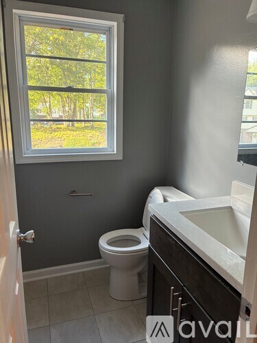 A bathroom with a toilet, sink, and a window.