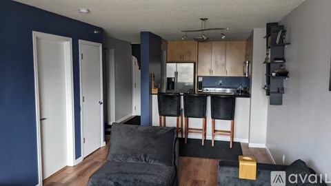 A living room with a grey couch and a kitchen area in the background.