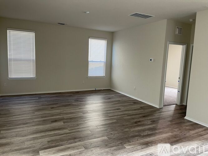 A spacious room with wooden flooring and two windows.