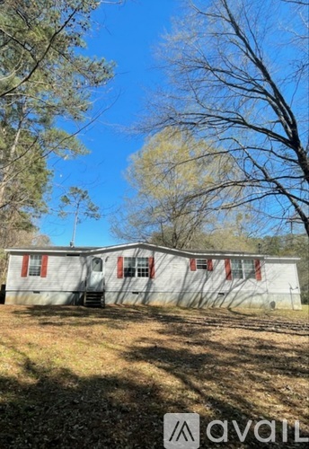 A white mobile home with a red stripe is surrounded by trees and grass.
