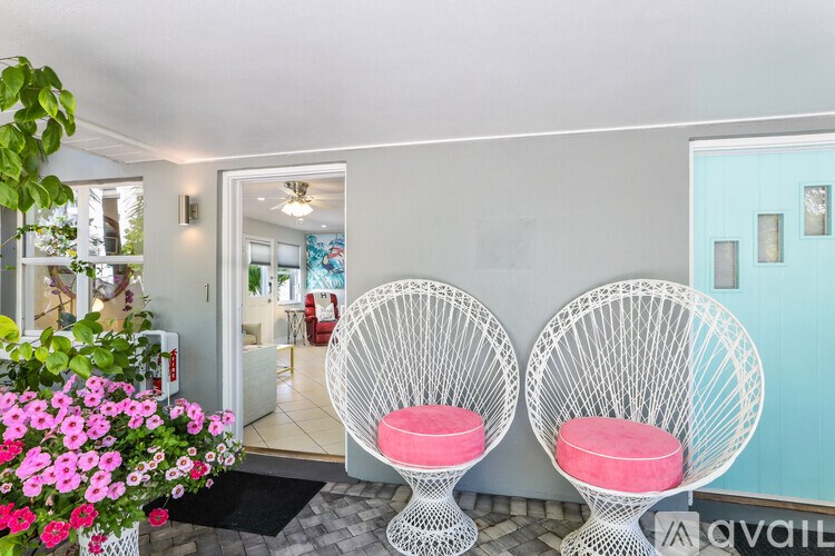Two white chairs with pink cushions are placed in front of a blue wall.