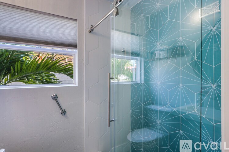 A bathroom with a glass shower door and a window with blinds.