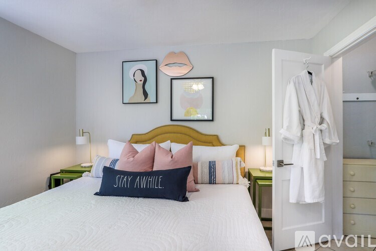A bedroom with a white bed and a "Stay Awhile" pillow.