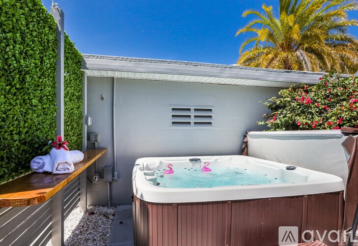 A hot tub with a pink flamingo float is in the foreground of a sunny backyard.