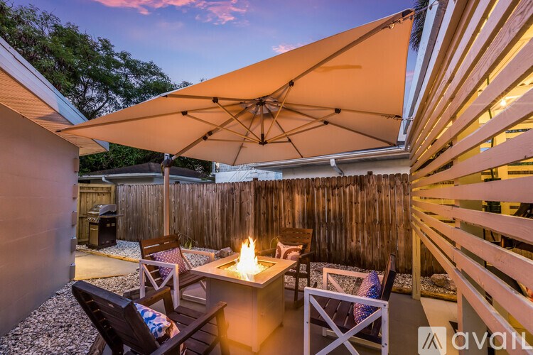 A patio with a fire pit and chairs under a large umbrella.