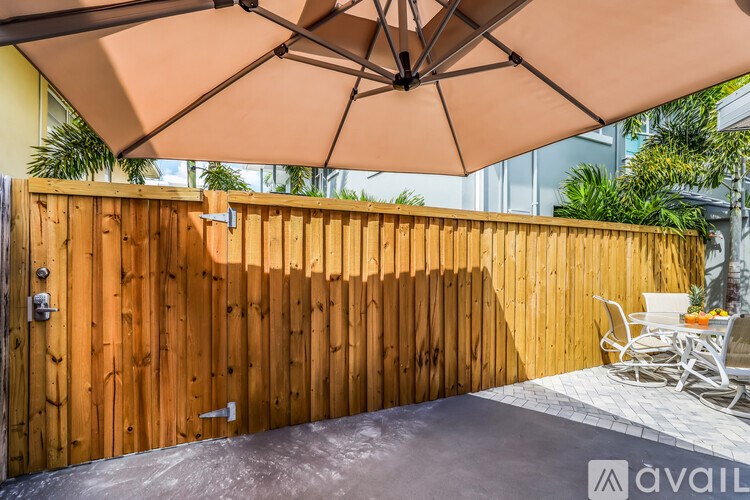 A wooden fence with a gate and a patio with chairs and an umbrella.