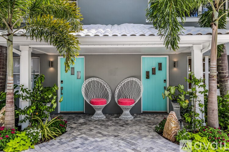 A white house with a blue door and a white chair with a red cushion.