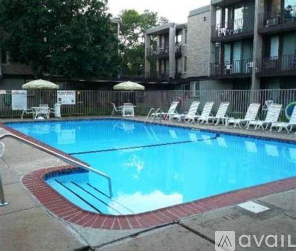 A pool with chairs around it and apartment buildings in the background.
