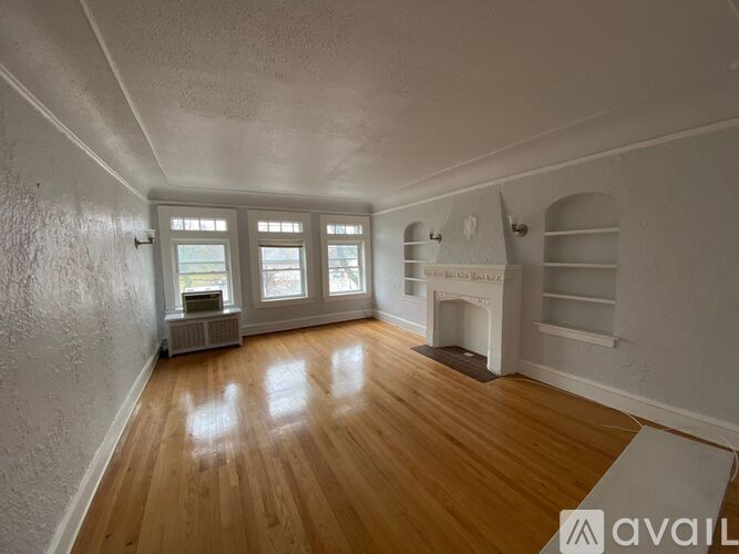 A room with wooden floors and white walls, featuring a fireplace and a window with a view.