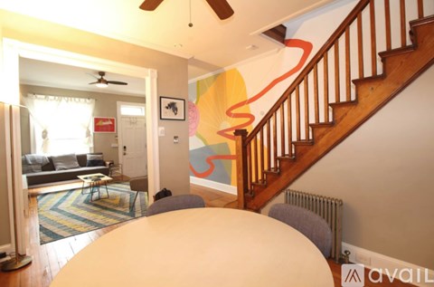 A living room with a couch, a rug, a table, a staircase, and a painting on the wall.