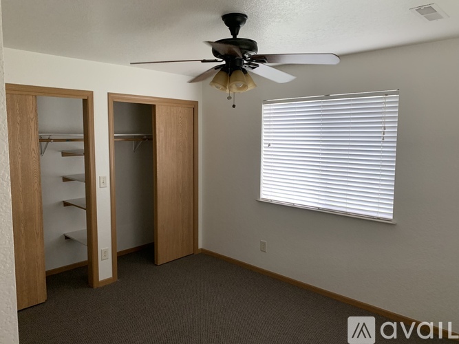A room with a ceiling fan, a window with blinds, and a closet with a mirror.