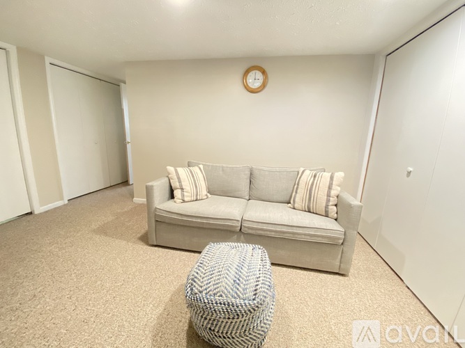 A living room with a grey couch and a round clock on the wall.