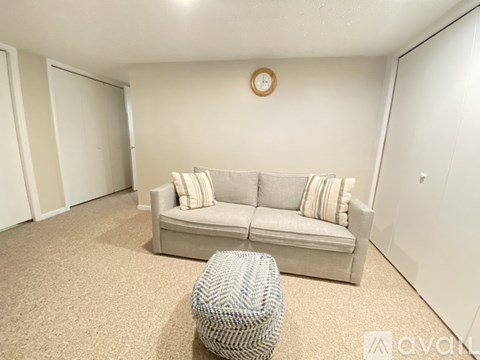 A living room with a grey couch and a round clock on the wall.