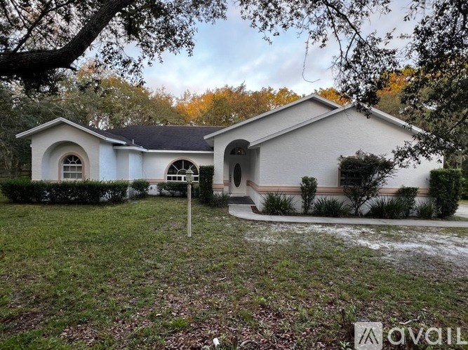 A white house with a black roof and a tree in front.