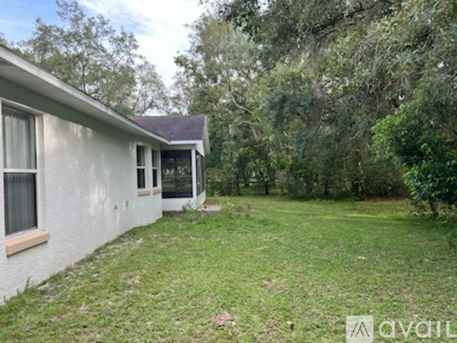 A house with a white exterior and a brown roof is surrounded by greenery.