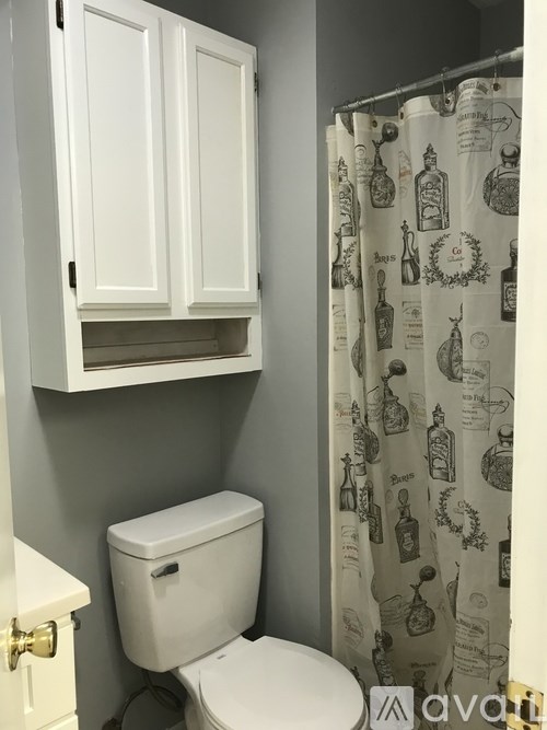 A white toilet with a cabinet above it and a shower curtain with bottles on it.