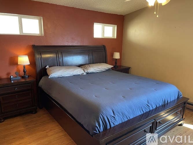 A bed with a blue comforter is in a room with wooden floors and two windows.