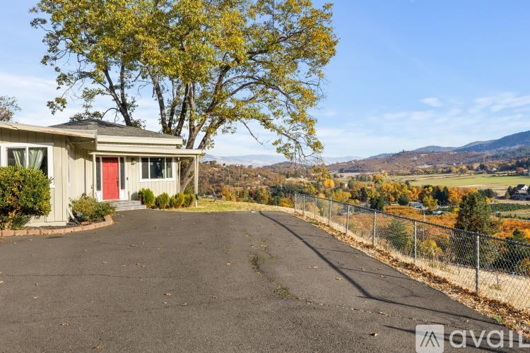 A house with a red door is surrounded by a fence and trees.