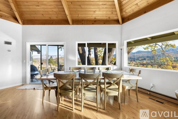 A wooden dining table with chairs is set up in a room with a view of the outdoors.