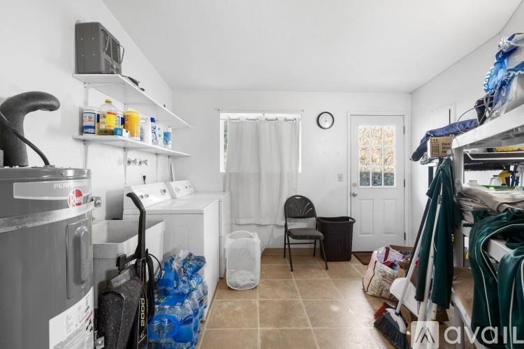 A black leather couch with a red pillow is in the center of a room with wooden floors and a stone wall.