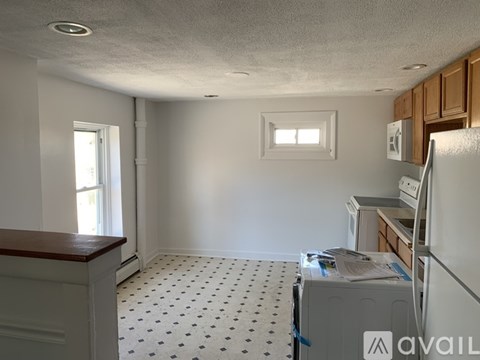 A kitchen with a white fridge, white cabinets, and a white wall with a window.