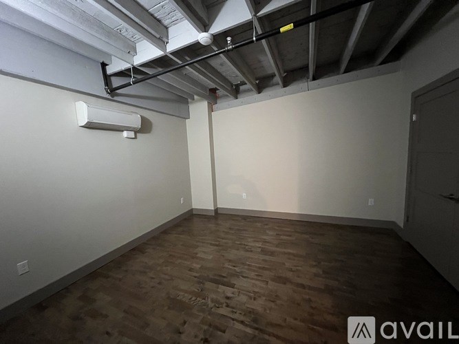 A room with wooden flooring and a white wall with a vent.