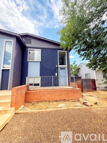 A blue house with a white door and windows is shown with a tree in the background.