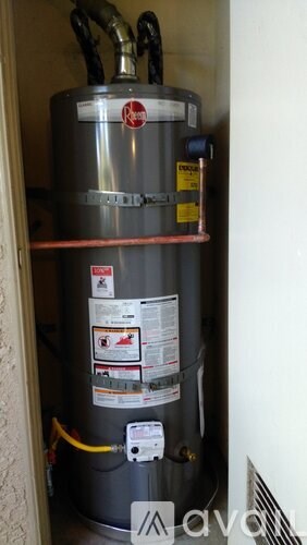 A water heater is installed in a narrow space between a wall and a door.