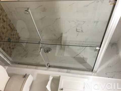 A shower with a glass door and a marble wall.