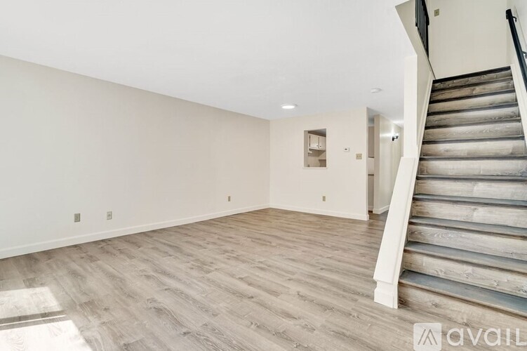 A spacious room with wooden flooring and a staircase on the right side.