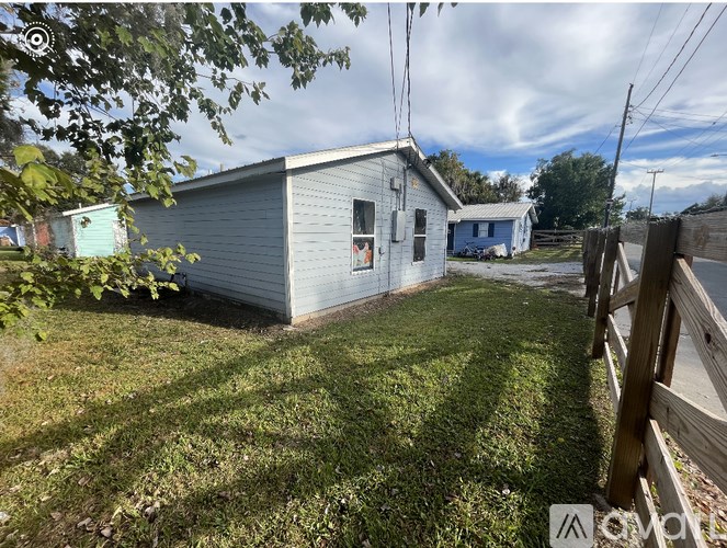 A small house with a grey roof and a white door is surrounded by a grassy area.