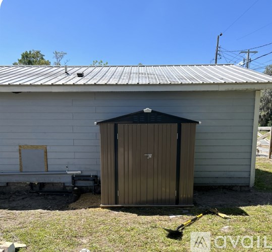 A shed with a brown door is situated in front of a white building.