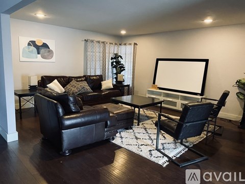A living room with a black leather couch and a white rug.